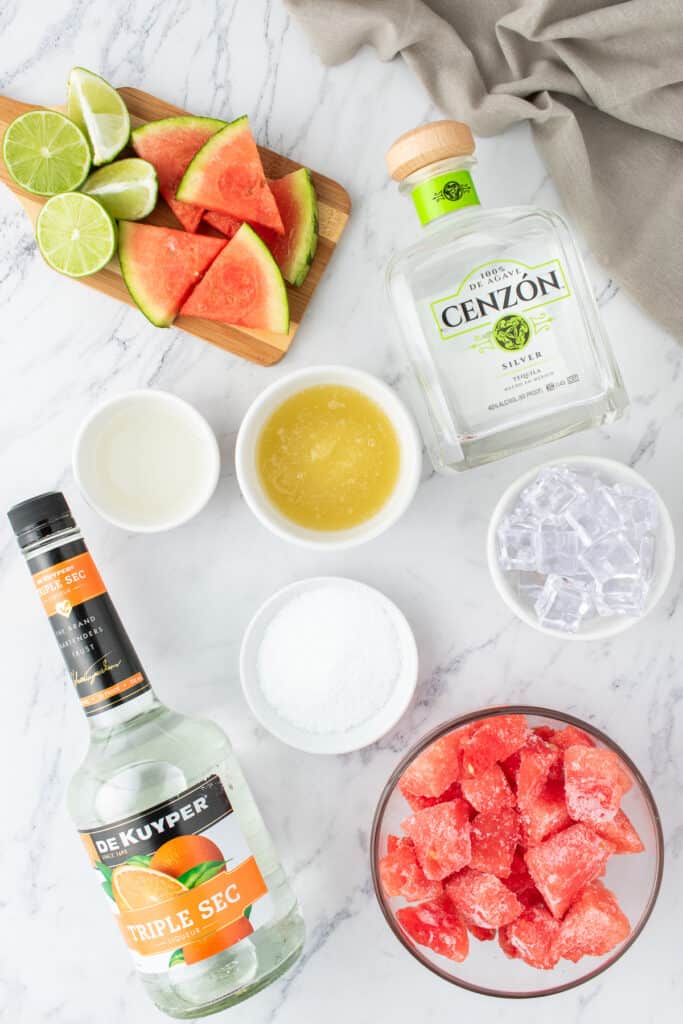 Overhead view of ingredients for watermelon margaritas, including tequila, triple sec, lime, and frozen watermelon
