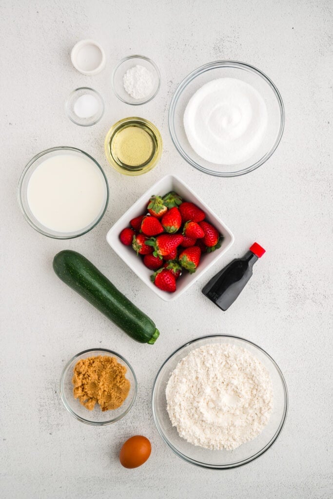 Overhead view of all ingredients for strawberry zucchini bread arranged on a white surface