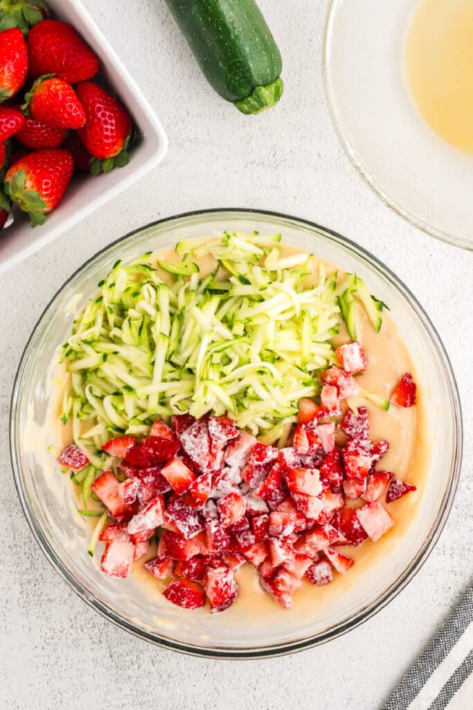 Bowl of strawberry zucchini bread batter topped with grated zucchini and floured diced strawberries