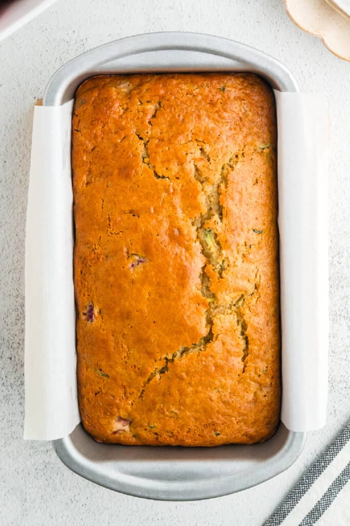 Golden-brown baked strawberry zucchini bread loaf still in the parchment-lined pan