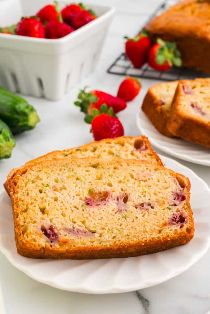 Close-up of sliced strawberry zucchini bread on a white plate with fresh strawberries in the background