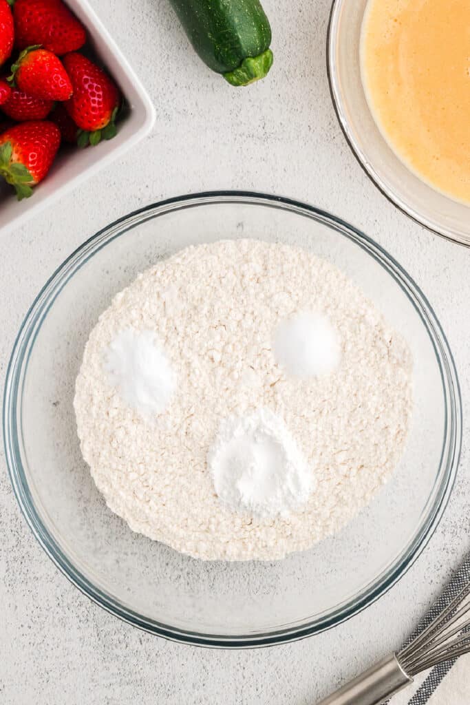 Dry ingredients including flour, baking powder, baking soda, and salt in a clear bowl