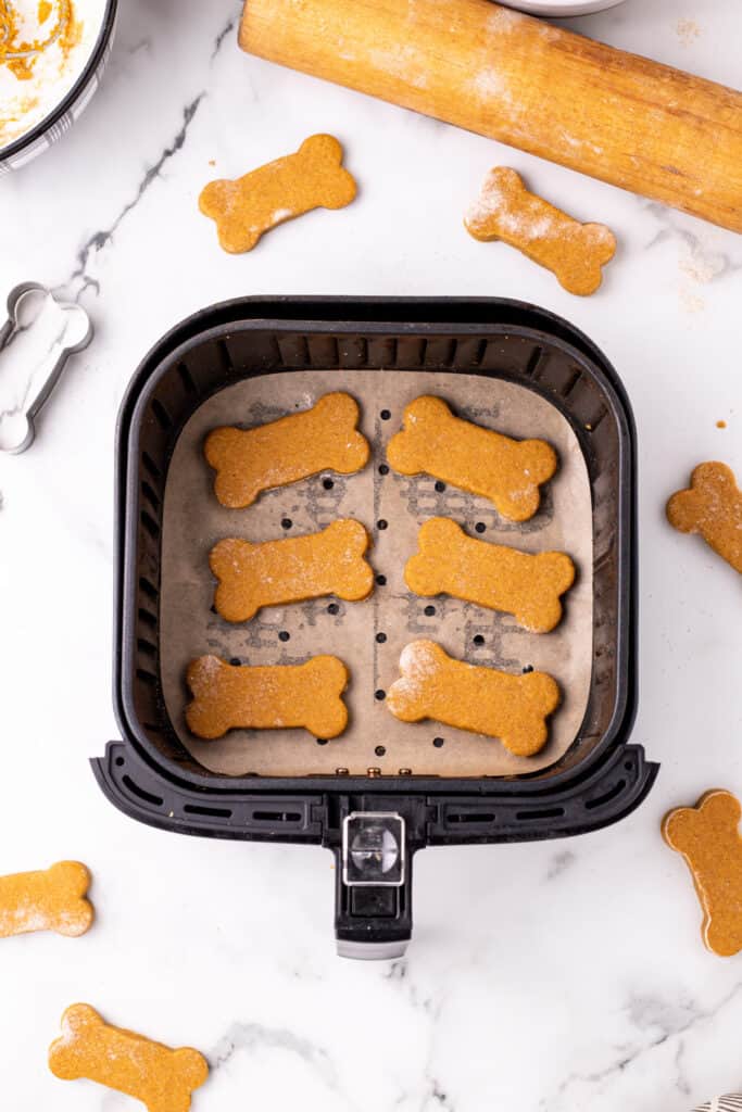 Bone-shaped dog treats placed inside an air fryer basket lined with parchment paper.