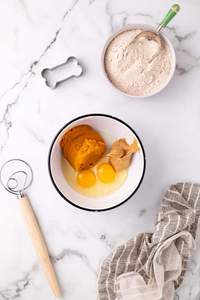 Pumpkin, eggs, and peanut butter combined in a white mixing bowl for dog treat dough.