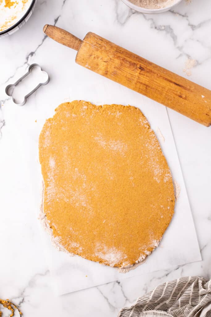 Rolled out dog treat dough on parchment paper with a vintage rolling pin.