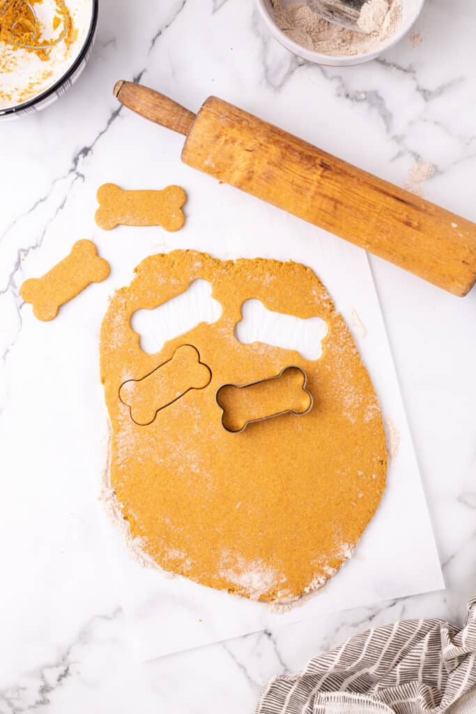 Bone-shaped cookie cutter cutting shapes out of pumpkin dog treat dough.