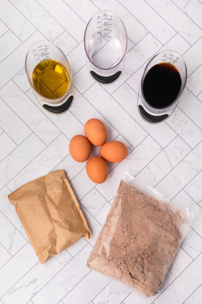Ingredients for Kahlua cake including eggs, oil, Kahlua, and dry cake mixes arranged on a marble surface.