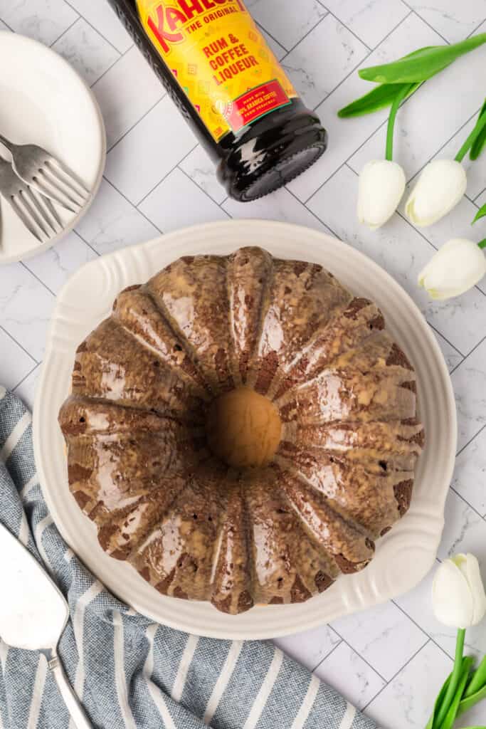 Finished Chocolate Kahlua Bundt Cake with glaze, Kahlua bottle, and white tulips.