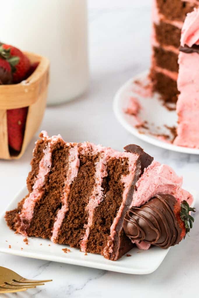 Close-up of a plated slice of chocolate strawberry cake with chocolate-covered strawberry garnish.