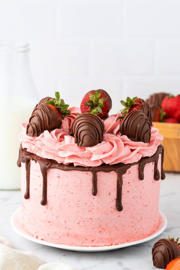 Whole chocolate strawberry cake decorated with pink buttercream, ganache drip, and chocolate-covered strawberries.