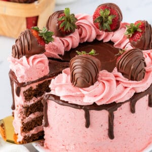 Close-up of a chocolate strawberry cake with pink strawberry buttercream, chocolate ganache drip, and chocolate-covered strawberries on top.