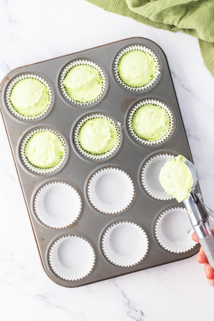Cupcake batter with green tint being scooped into a lined muffin pan