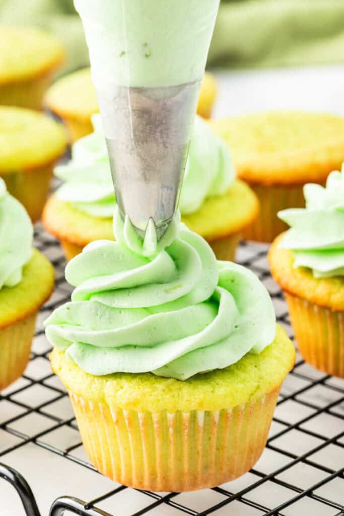 Close-up of piping light green lime frosting onto a coconut cupcake
