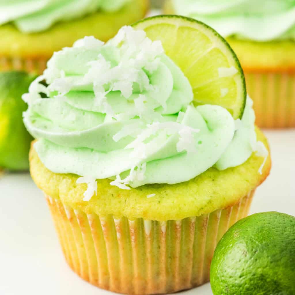 Bright and fluffy coconut lime cupcake with green frosting, lime slice, and shredded coconut on top