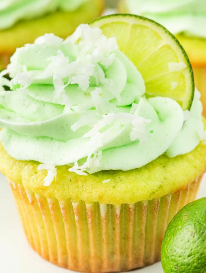 Bright and fluffy coconut lime cupcake with green frosting, lime slice, and shredded coconut on top