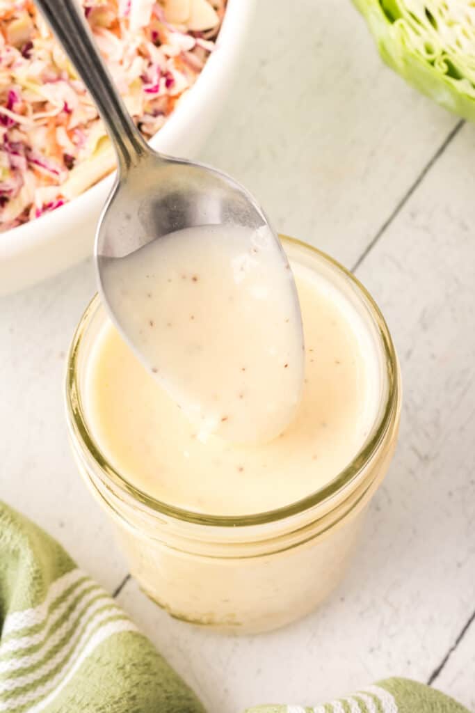 This Coleslaw Dressing has the perfect balance between tangy and sweet. Pour it over pre-shredded cabbage or use your own mix of cabbage and carrots for the perfect side dish any time! Spoonful of creamy coleslaw dressing held over a jar, ready for serving.
