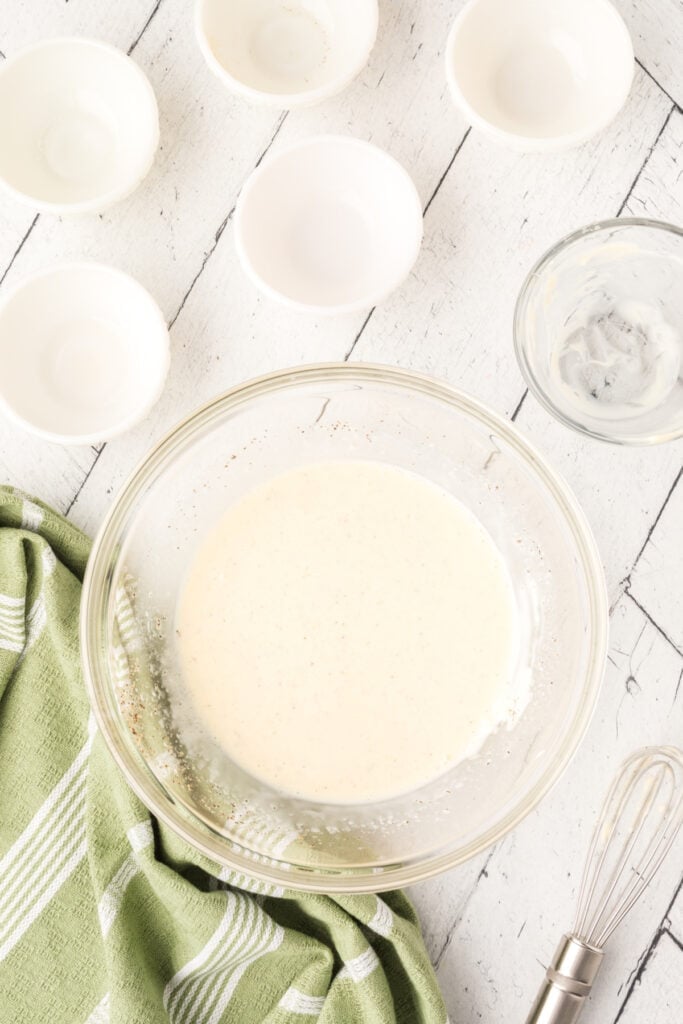 Whisked homemade coleslaw dressing in a glass bowl next to a green cloth.