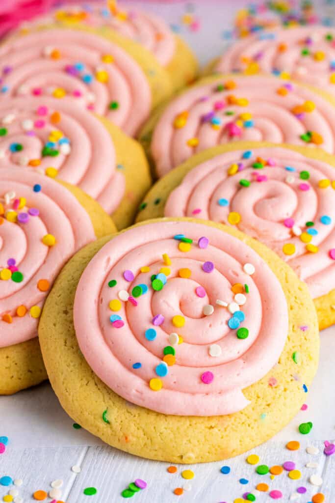 Stack of frosted confetti cookies with pink frosting and colorful sprinkles on top.