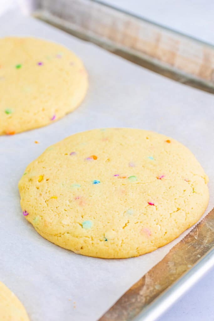 Baked unfrosted confetti cookies cooling on a parchment-lined baking sheet.