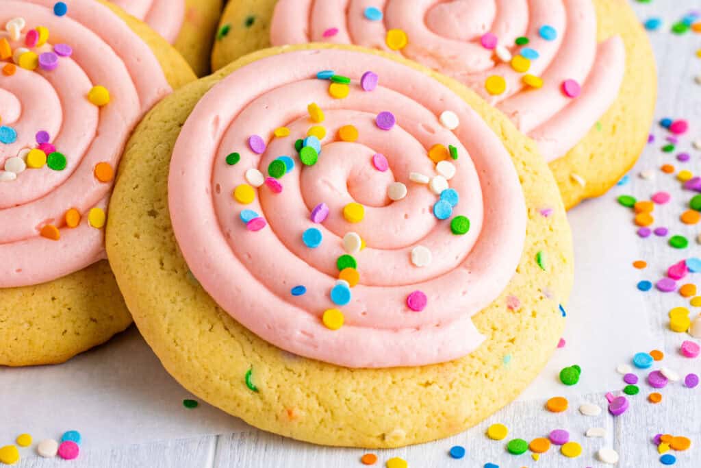 Several frosted confetti cookies topped with colorful sprinkles scattered on white surface.