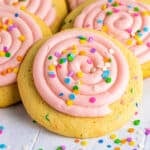 Close-up of a frosted confetti cookie with a swirl of pink frosting and bright sprinkles.