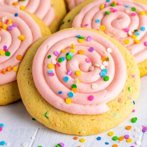 Close-up of a frosted confetti cookie with a swirl of pink frosting and bright sprinkles.