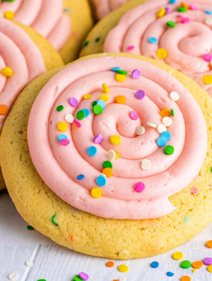 Close-up of a frosted confetti cookie with a swirl of pink frosting and bright sprinkles.