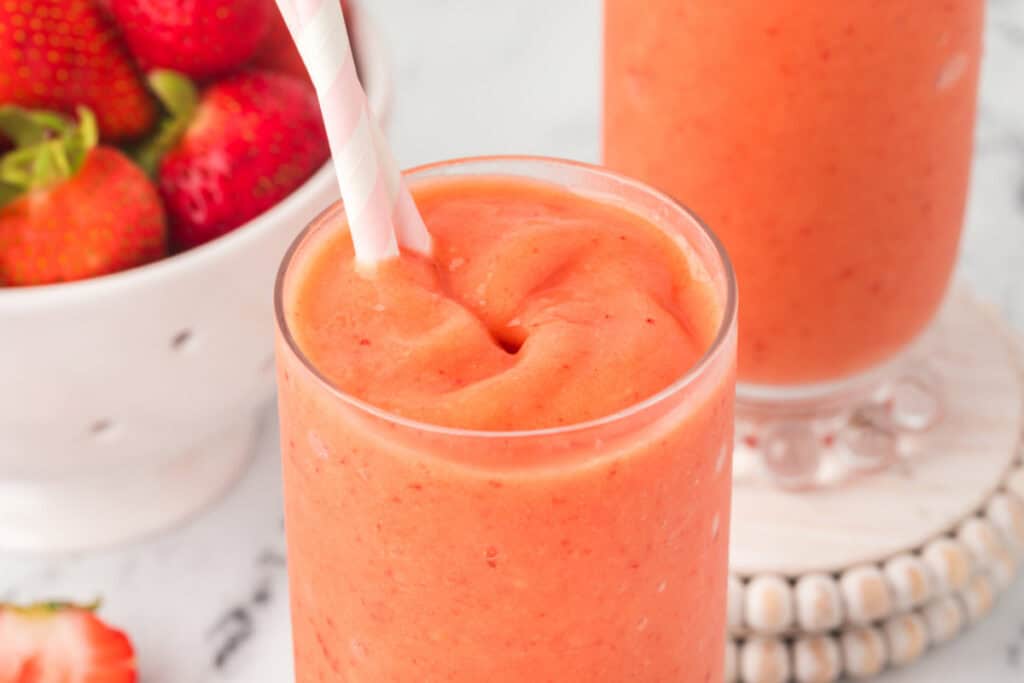 Two glasses of sunrise sunset smoothie with pink straws and fresh strawberries in the background.