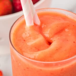 Close-up square image of sunrise sunset smoothie with pink and white striped straw.