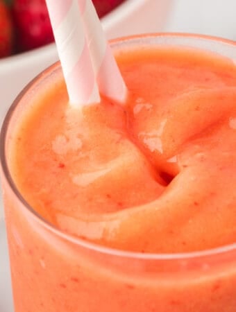 Close-up square image of sunrise sunset smoothie with pink and white striped straw.
