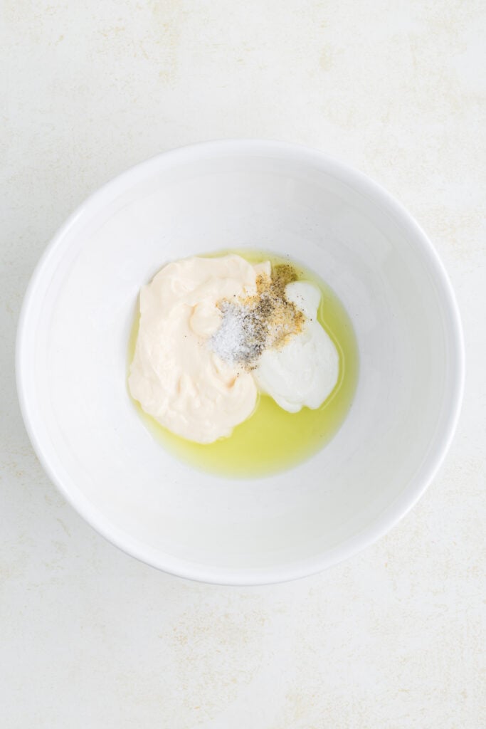 Ingredients for the dressing including mayo, yogurt, pickle juice, and seasonings in a white bowl.