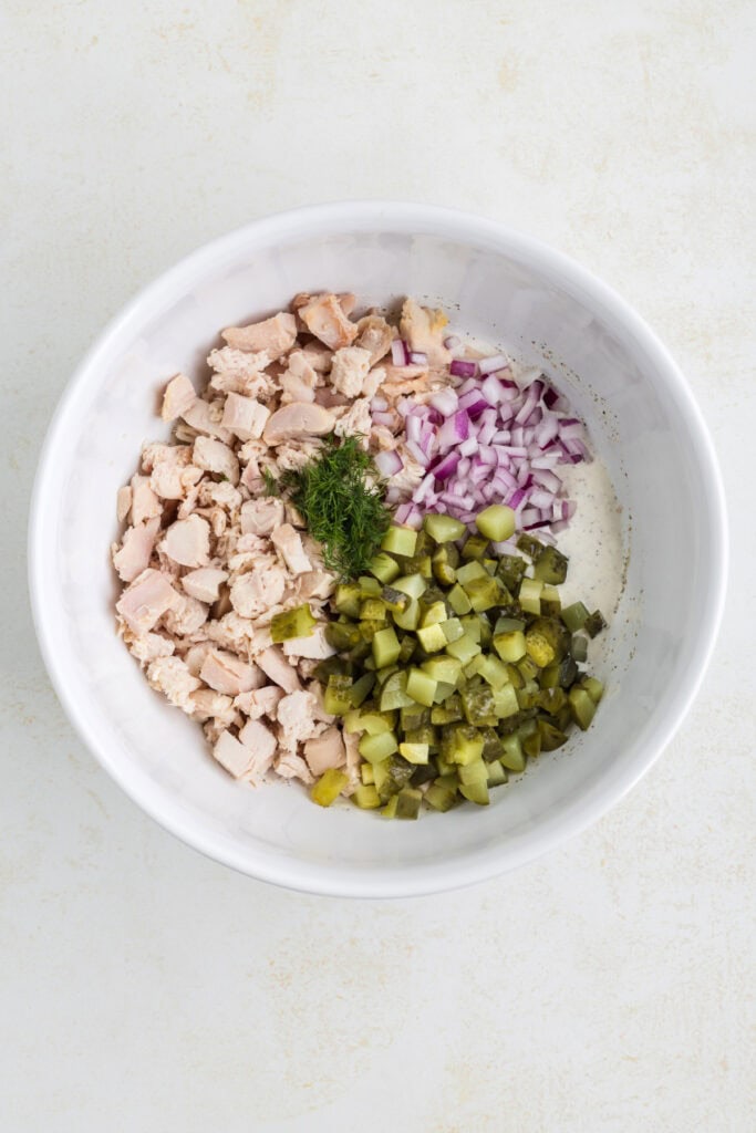Chopped chicken, red onion, dill pickles, and fresh dill in a bowl with dressing.