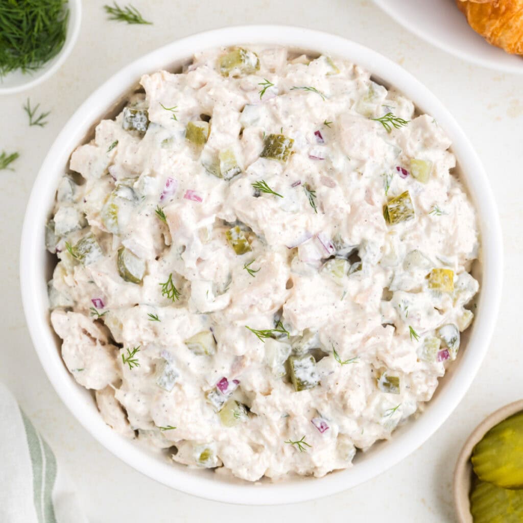 Square crop of dill pickle chicken salad in a white bowl, garnished with dill.