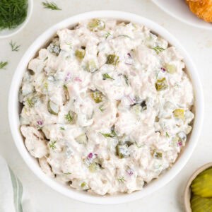 Square crop of dill pickle chicken salad in a white bowl, garnished with dill.