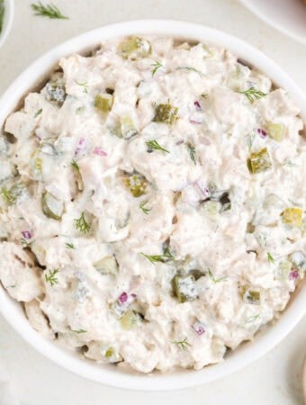 Square crop of dill pickle chicken salad in a white bowl, garnished with dill.