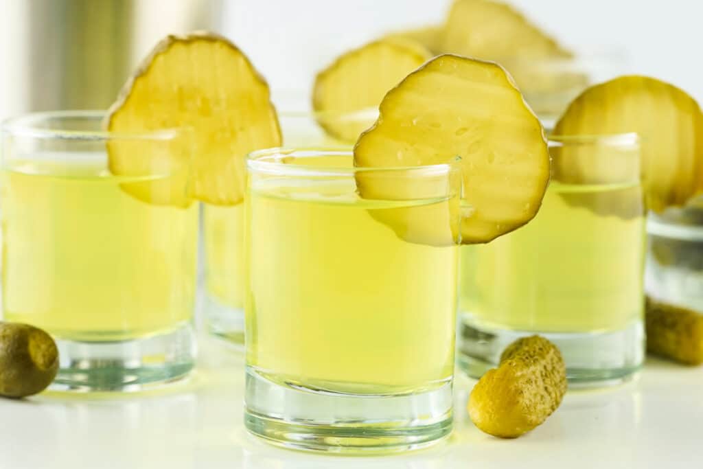 Side view of pickle shots arranged together with gherkins scattered around