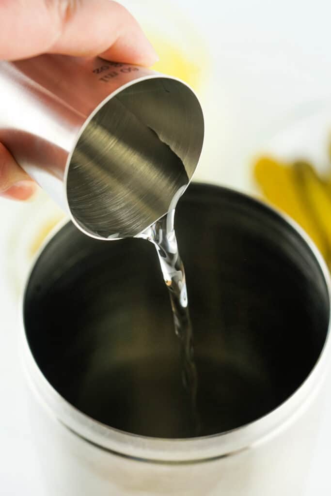 Measuring jigger pouring vodka into a cocktail shaker for pickle shots