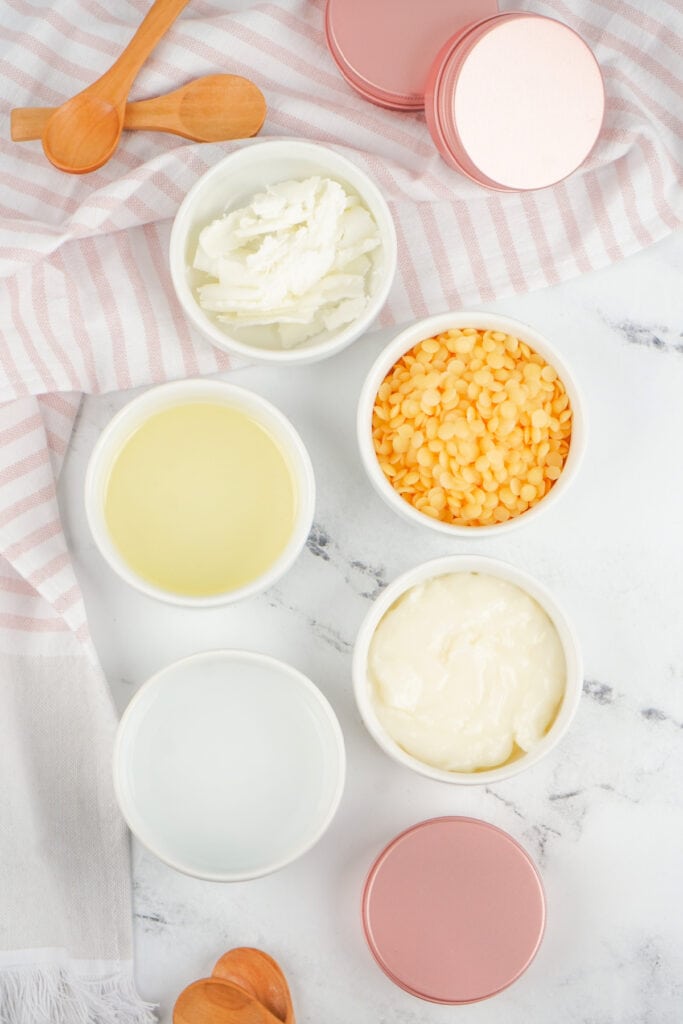 Ingredients for dog paw balm arranged in small white bowls with wooden spoons and pink metal tins.