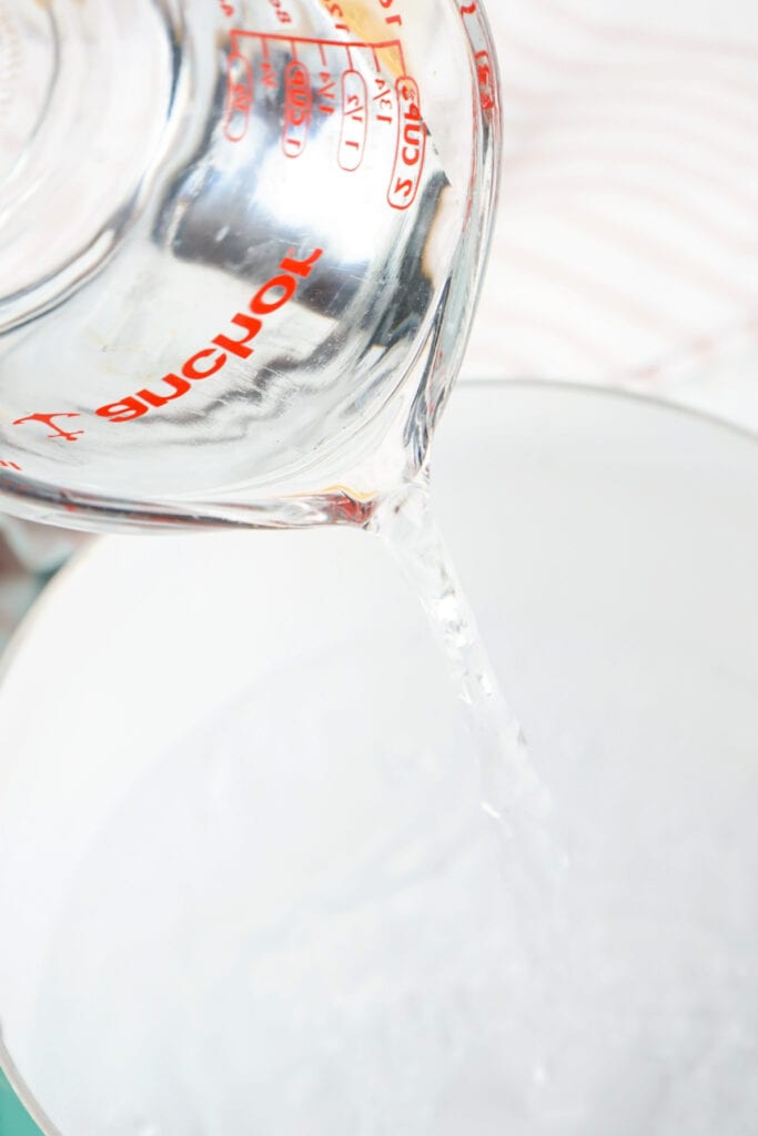 Water being poured from a glass measuring cup into a saucepan for melting ingredients.