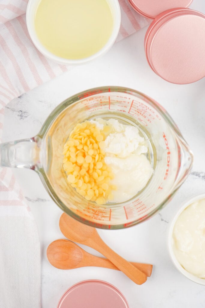 Beeswax pellets, coconut oil, and shea butter combined in a measuring cup, ready for melting.
