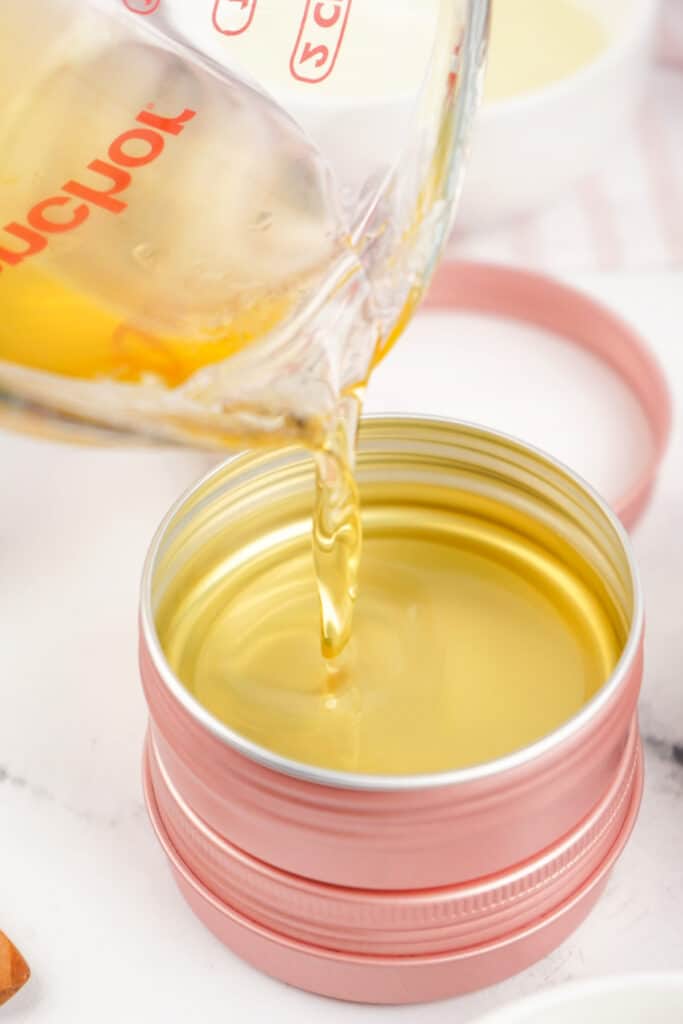 Hot melted balm being poured into a pink metal tin container.