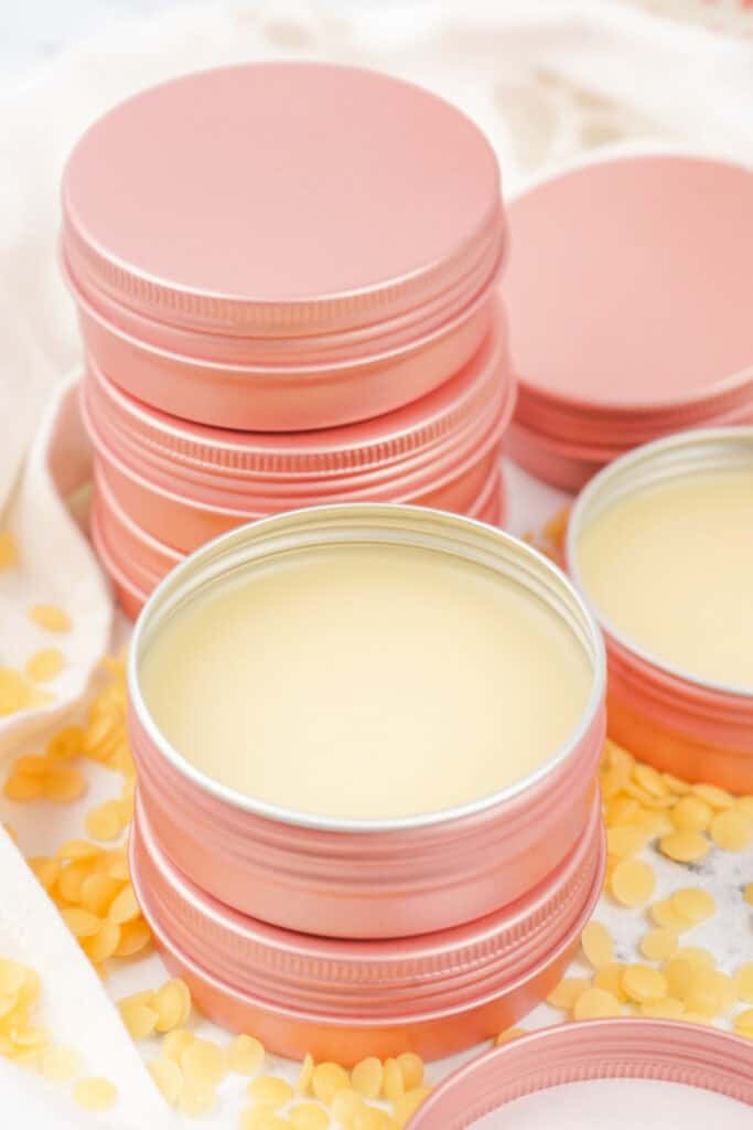 Stack of pink tins filled with finished dog paw balm, surrounded by beeswax pellets.