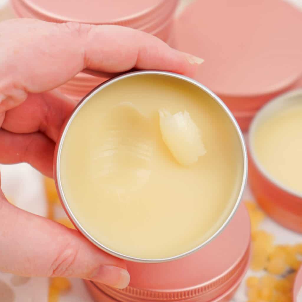 Close-up of a hand holding a tin of dog paw balm with a creamy, smooth surface.