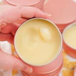 Close-up of a hand holding a tin of dog paw balm with a creamy, smooth surface.