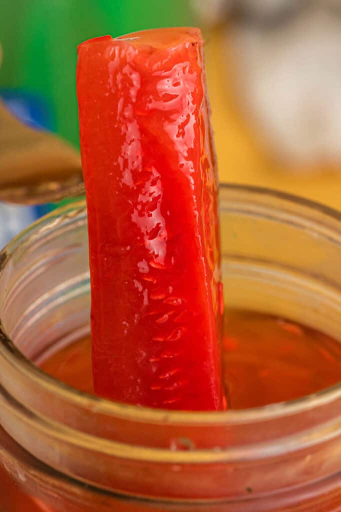 Close-up of a bright red Kool-Aid pickle being lifted from a jar.