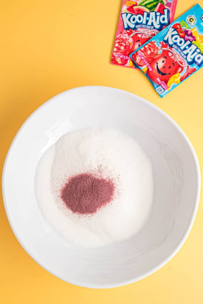 Bowl of sugar with a mound of Kool-Aid powder on top, Kool-Aid packets in the background.