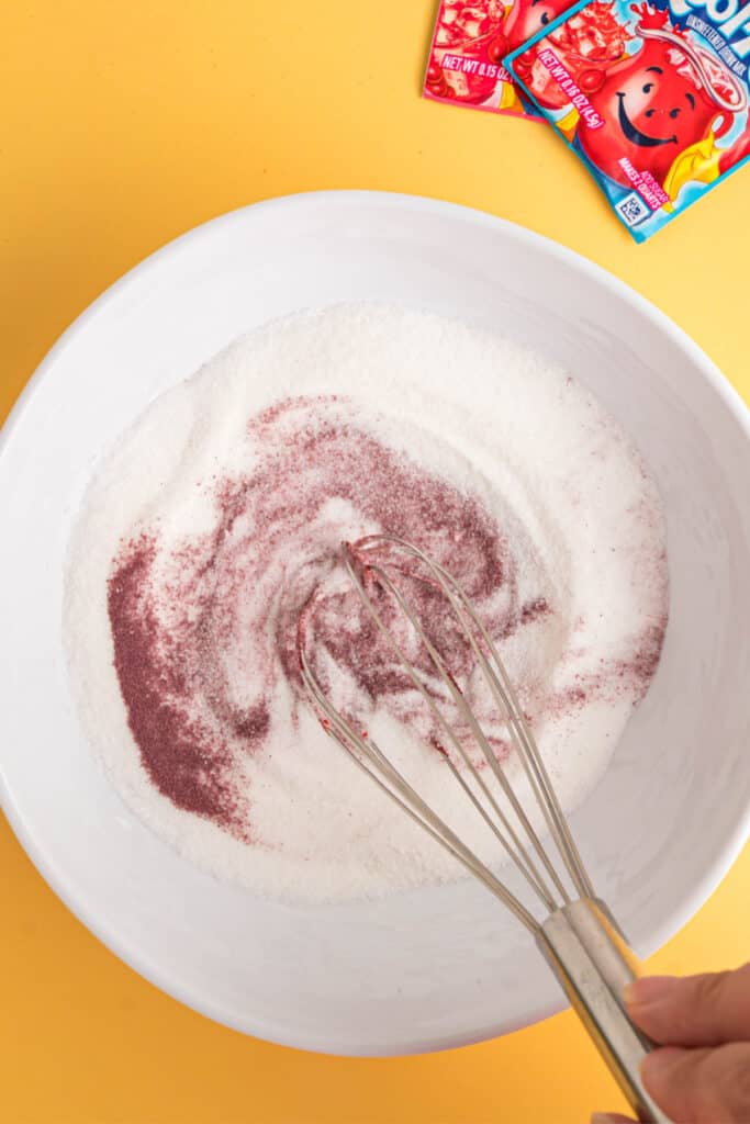 Whisk mixing sugar and Kool-Aid powder in a white bowl.