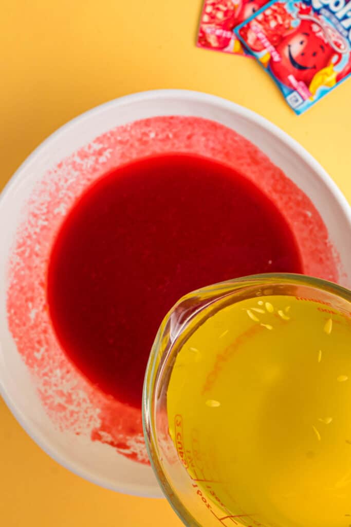 Pickle brine being poured into the bright red Kool-Aid mixture.