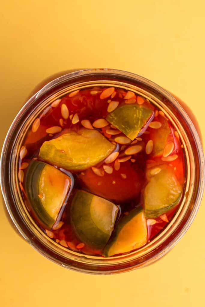 Pickles soaking in vibrant red Kool-Aid brine inside a glass jar.