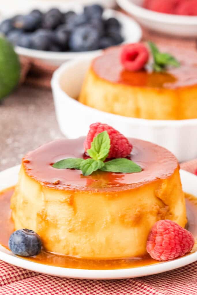 Mini caramel flan served on a white plate with caramel sauce, garnished with raspberry and mint.
